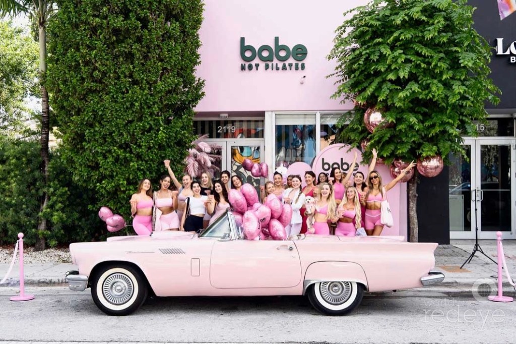 women in pink athleisure post in front of a pink convertible in front of a pink building with a logo reading, "Babe Hot Pilates"