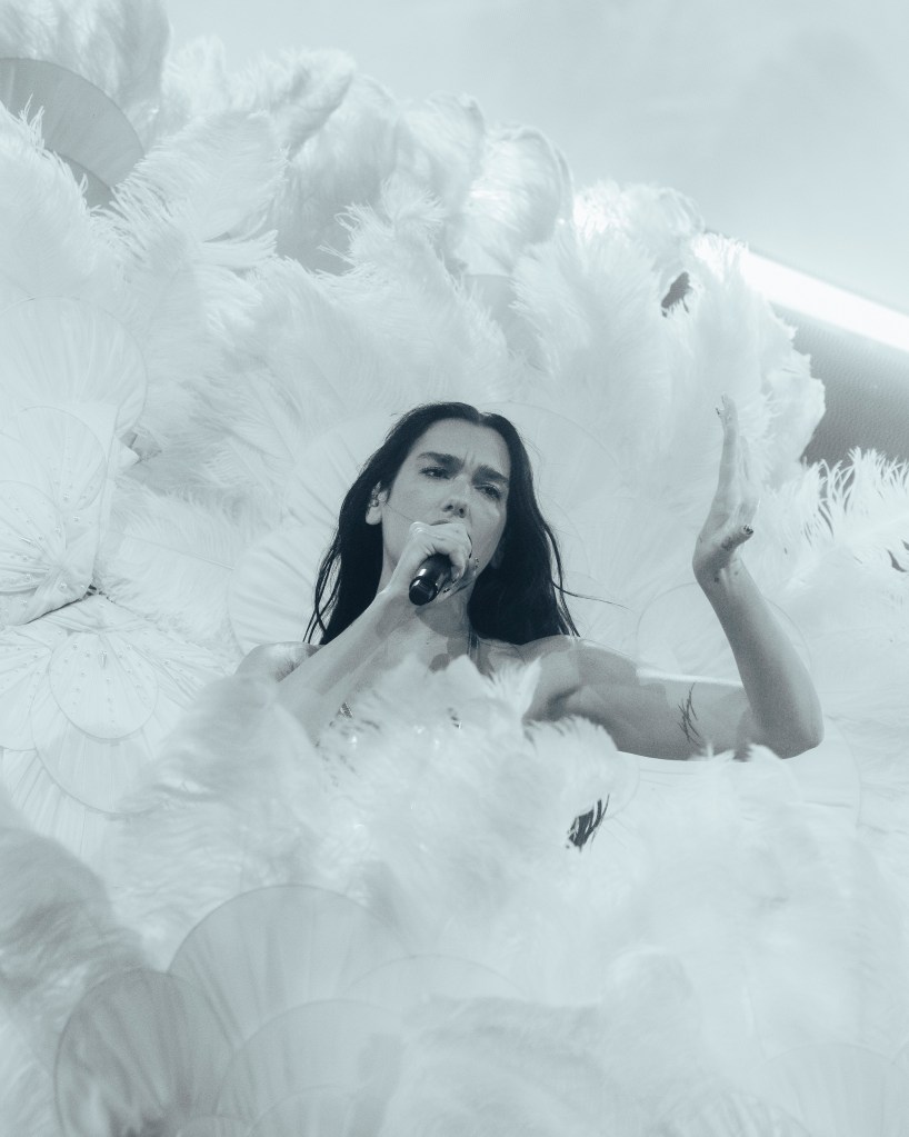 Dua Lipa surrounded by white feathers. 
