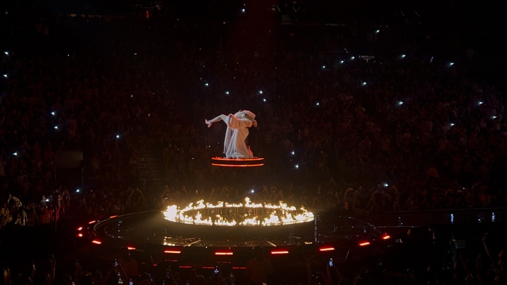 Dua lipa on stage elevated and surrounded by a ring of fire. 