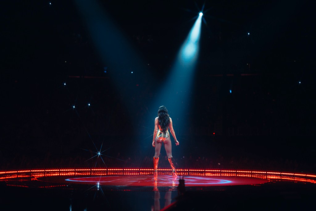 Picture of dua Lipa standing on a big stage with black and red lights .