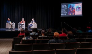 a panel of filmmakers speaks on a stage in front of an audience in a theater
