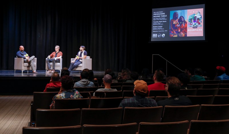 a panel of filmmakers speaks on a stage in front of an audience in a theater