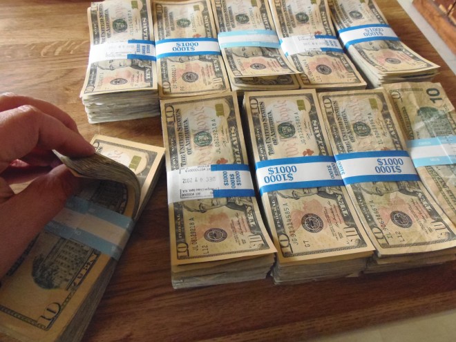 a hand counts a stack of money on a table with other stacks of money