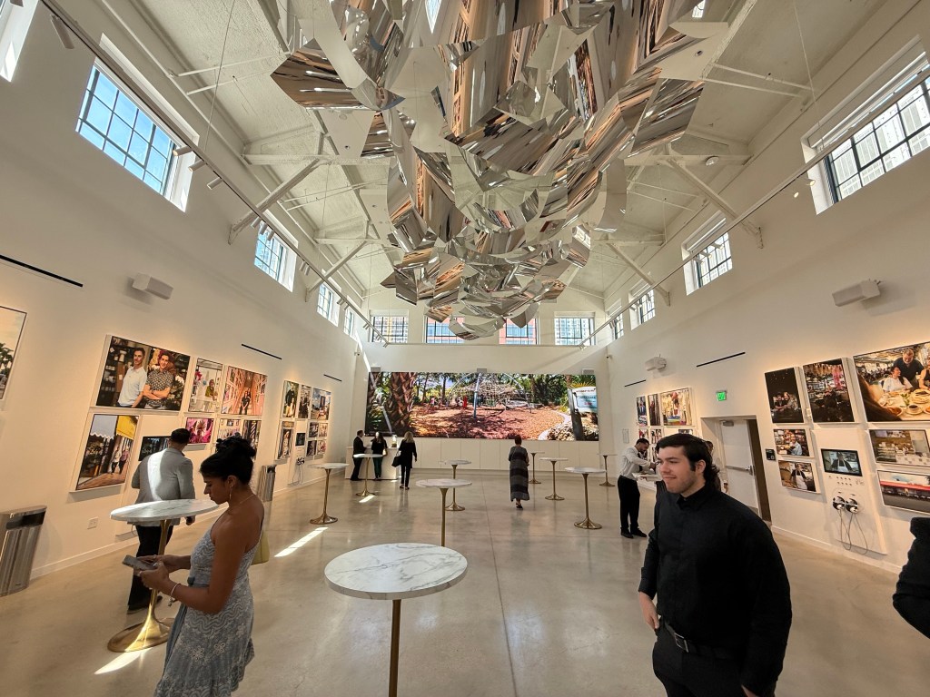 people walk around an art gallery with art on the walls and a sculpture hanging on the roof