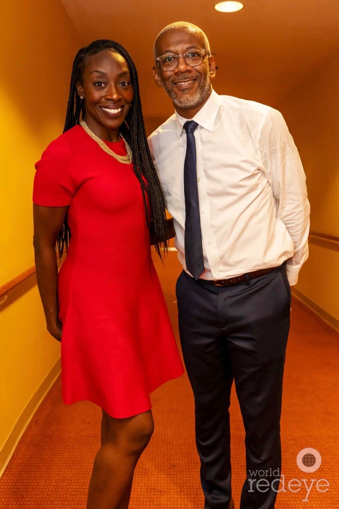 a woman in a red dress and a man in a suit pose in a hallway