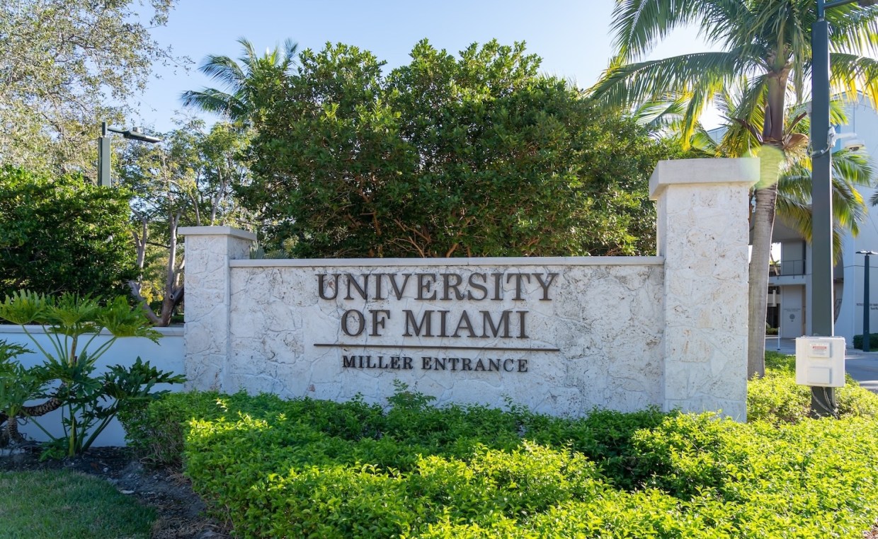 white stone wall on the UM campus with lettering that says: "UNIVERSITY OF MIAMI MILLER ENTRANCE"