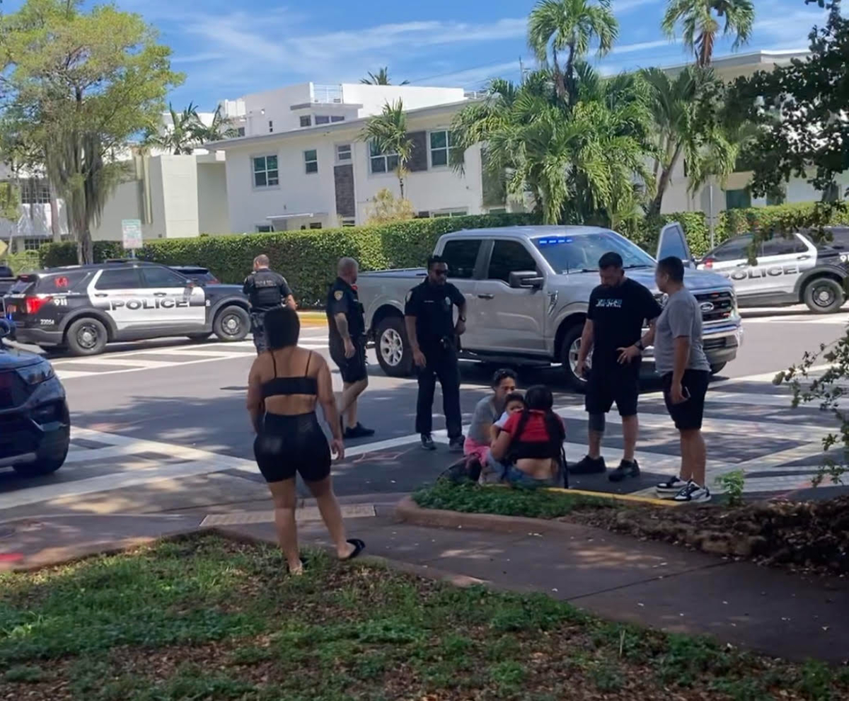Miami Beach intersection, where an unmarked police car sits at an intersection and pedestrians surround a woman on the floor