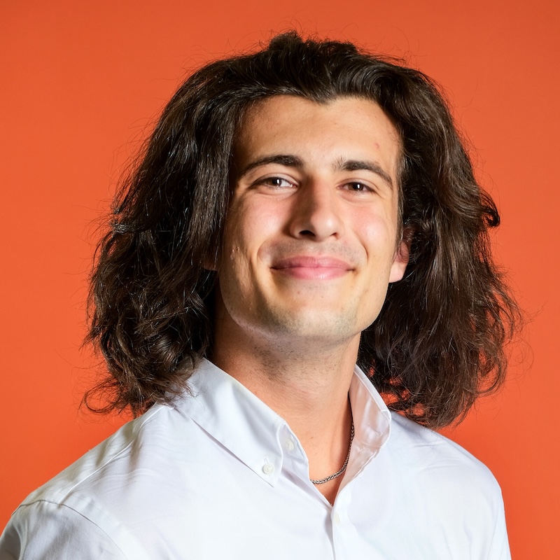 smiling young man with long hair against an orange background