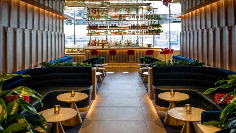 sleek airport lounge with bar in the background and plush blue booths in the foreground