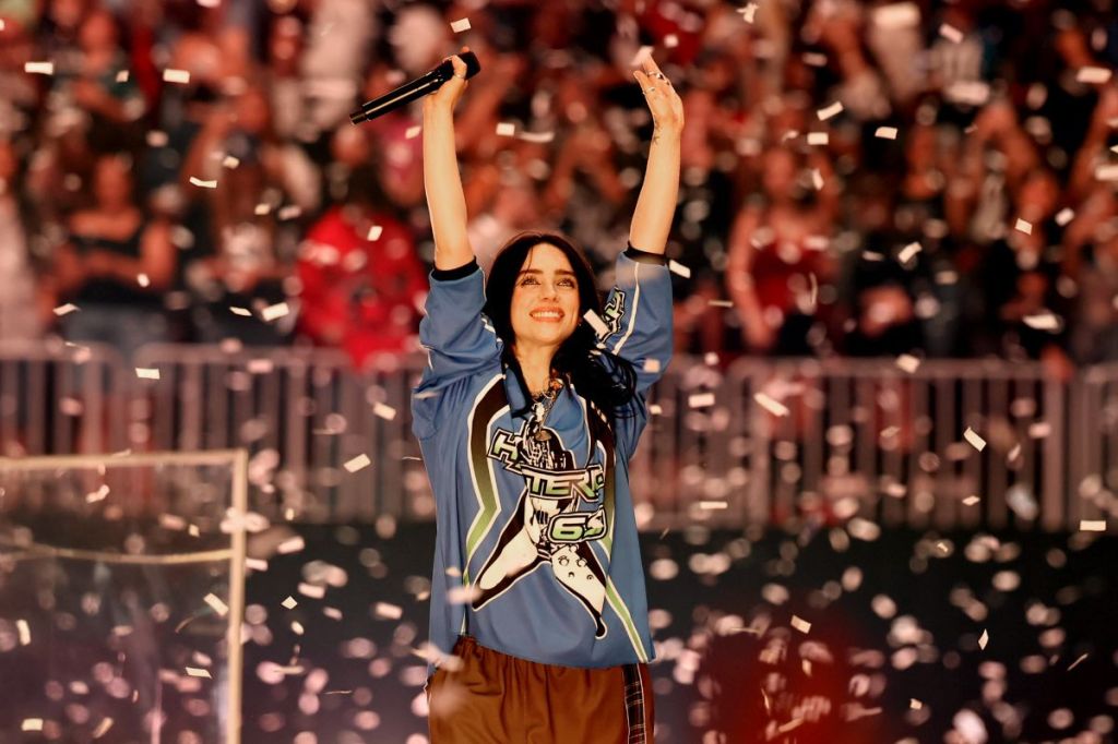 Picture of Billie Eilish on stage with her hands up, surrounded by confetti.