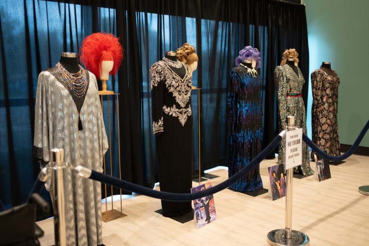 dresses on mannequins and wigs on display in front of a curtain