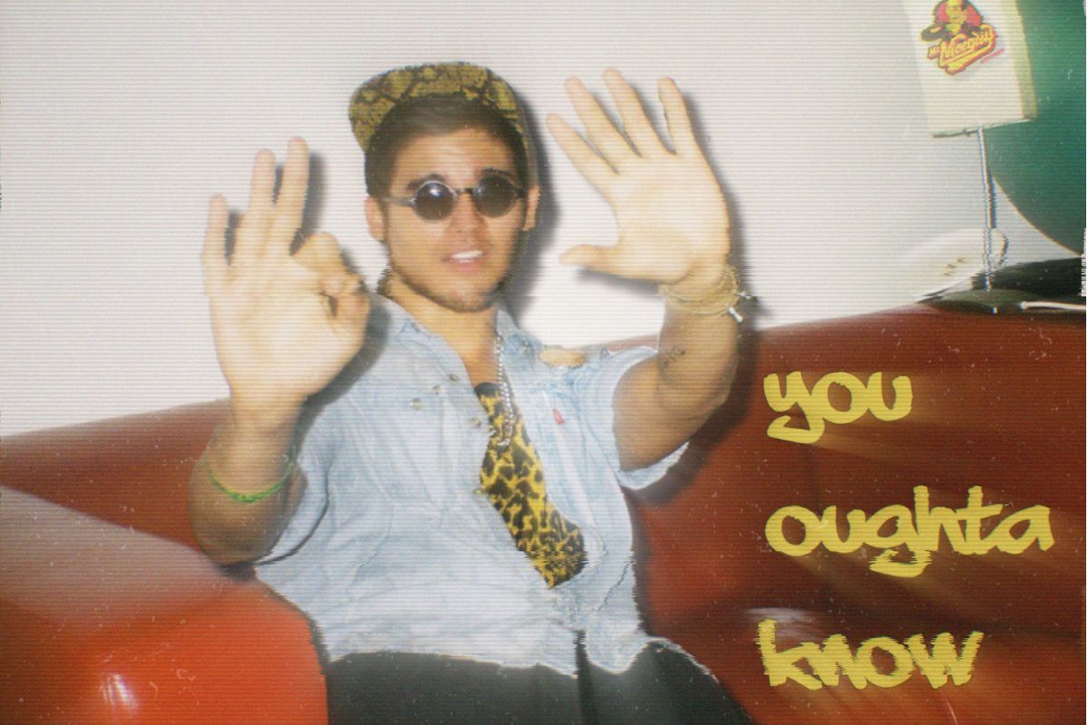 Image of a young man sitting on a red couch wearing glasses.