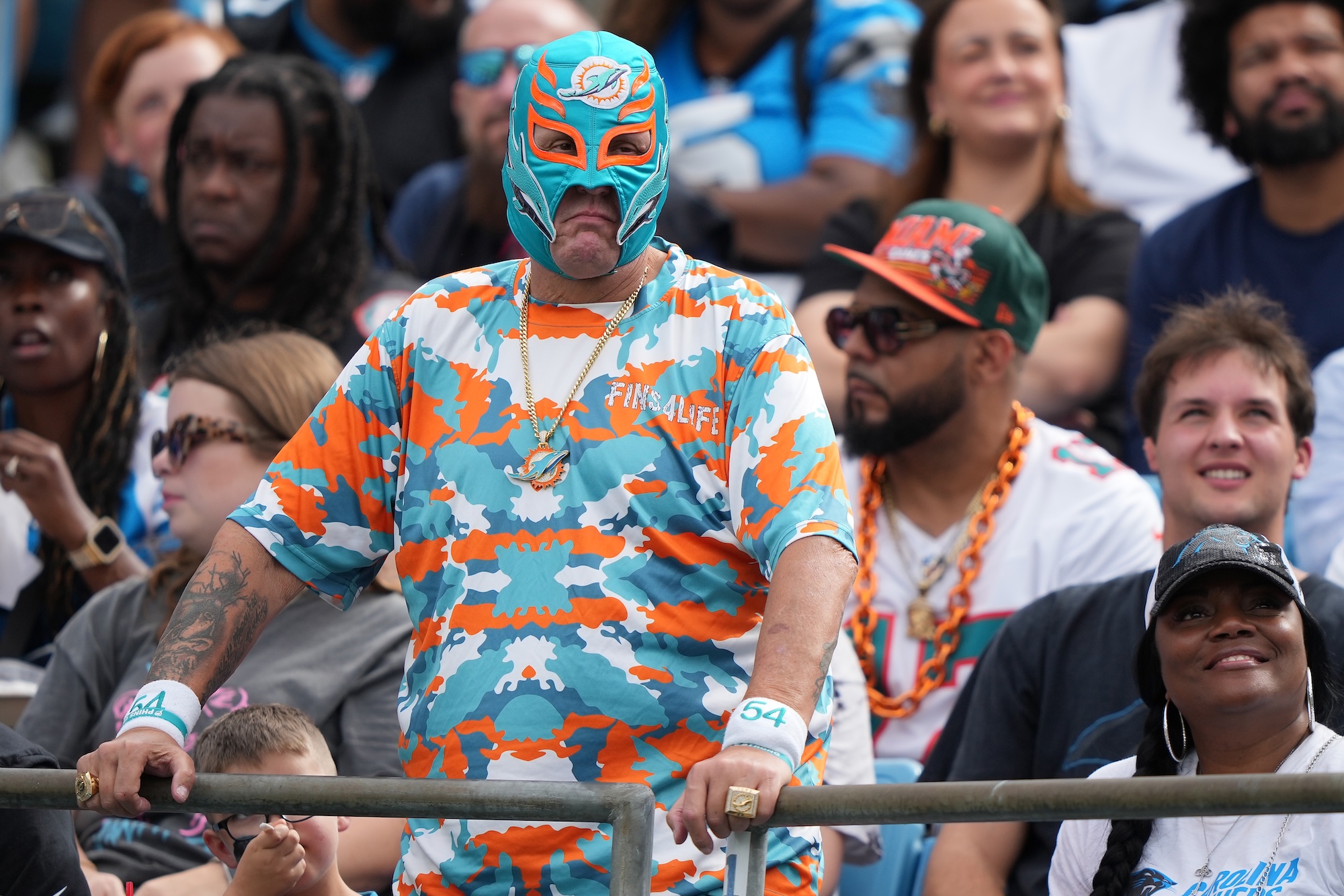 a Miami Dolphins fan dressed in a team-themed superhero costume and mask looks on in dismay at Bank of America Stadium in Charlotte, North Carolina, on October 05, 2025.