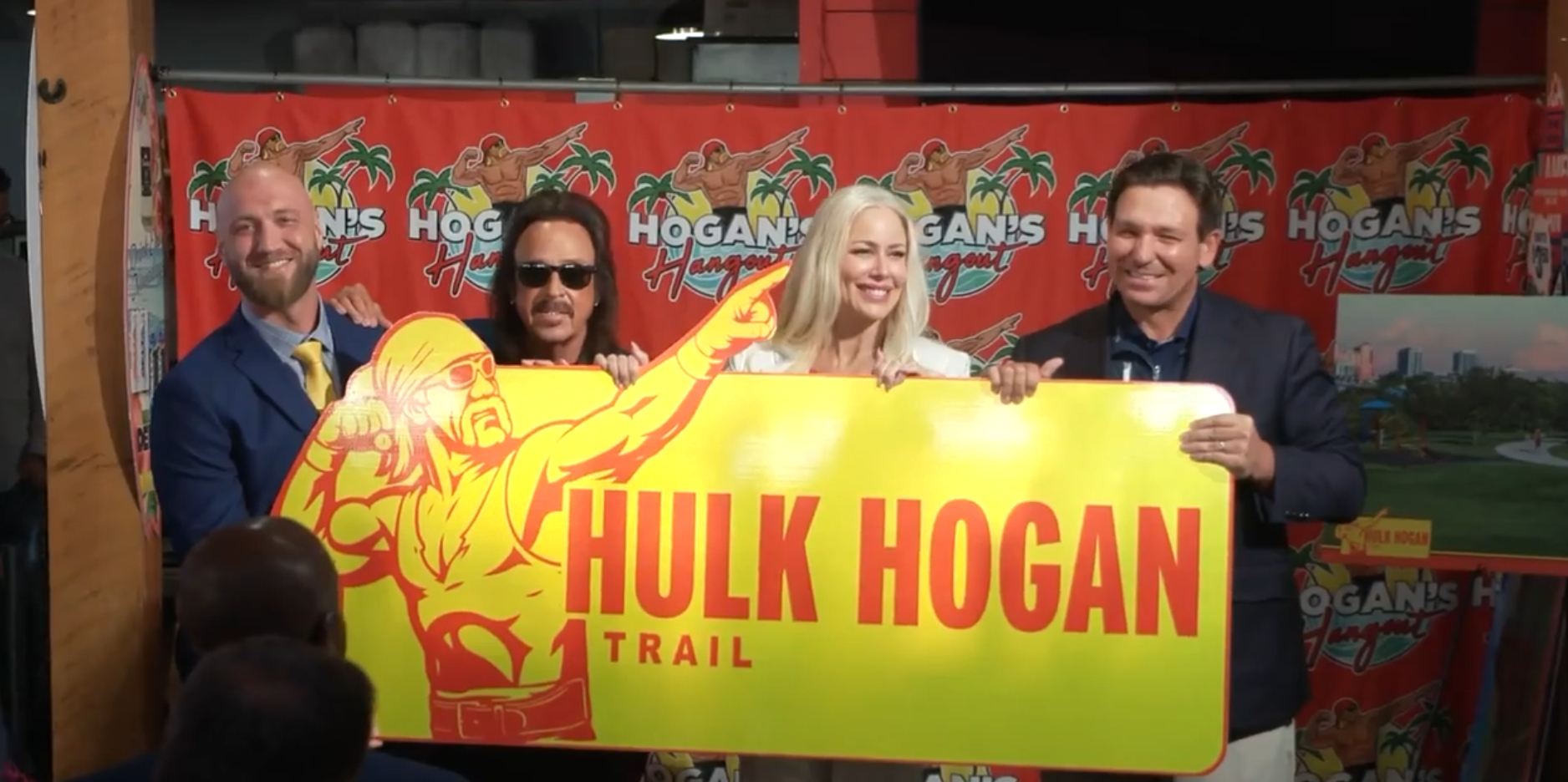 Ron DeSantis (far right) poses with Hulk Hogan's family and James Hart pose with Yellow and Red Hulk Hogan trail sign
