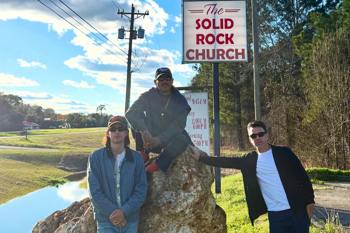 Image of three men posing for the camera by a green field