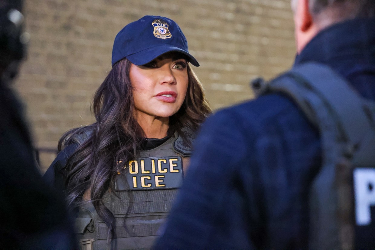 Kristi Noem wearing police, ICE vest and a blue baseball hat speaking to a law enforcement officer