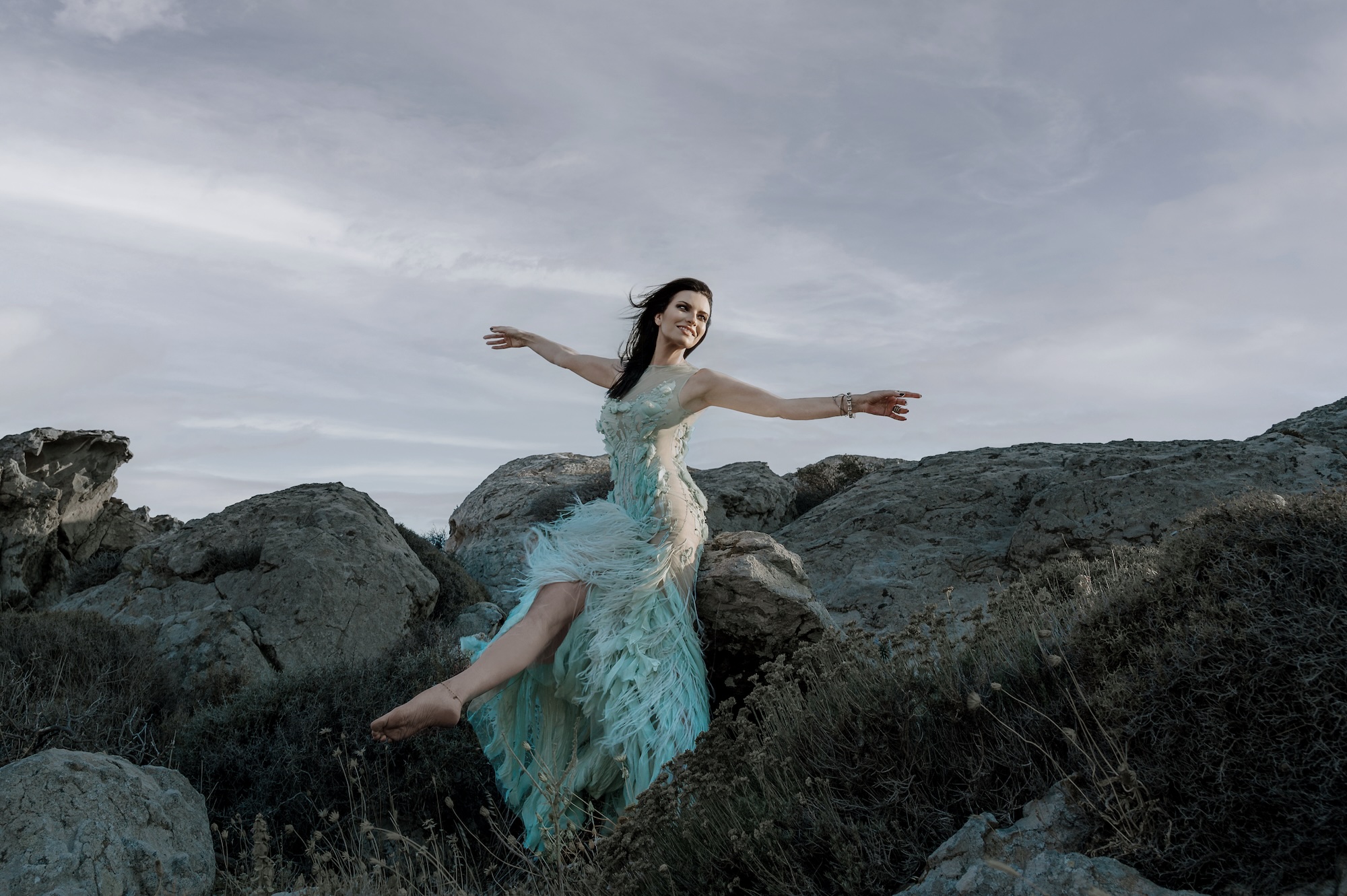 Picture of a woman sitting on a rock wearing a light blue dress.