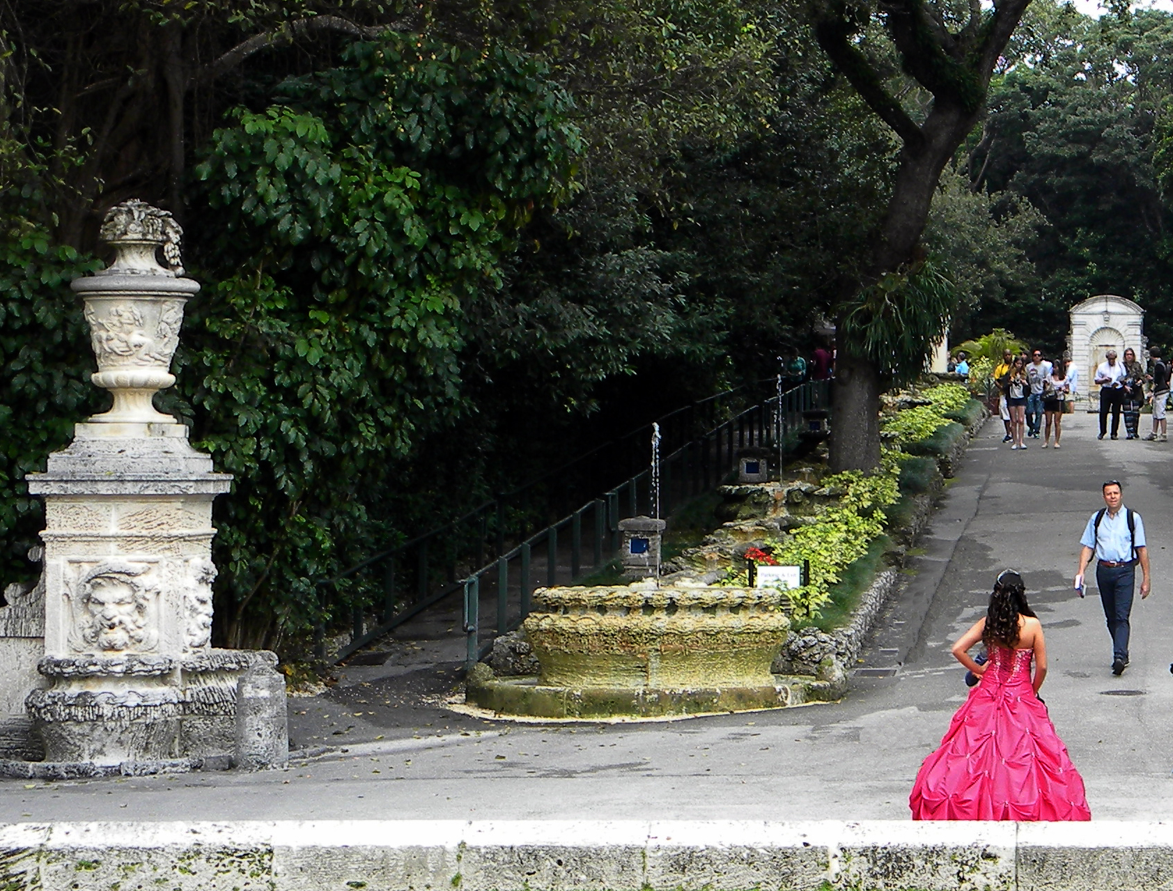 a girl in a hot pink quinceañera dress walks the gardens of an estate