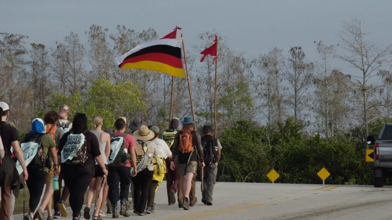 A group of people on a prayer walk through the Everglades; the person in the front holds up the Miccosukee Tribe flag