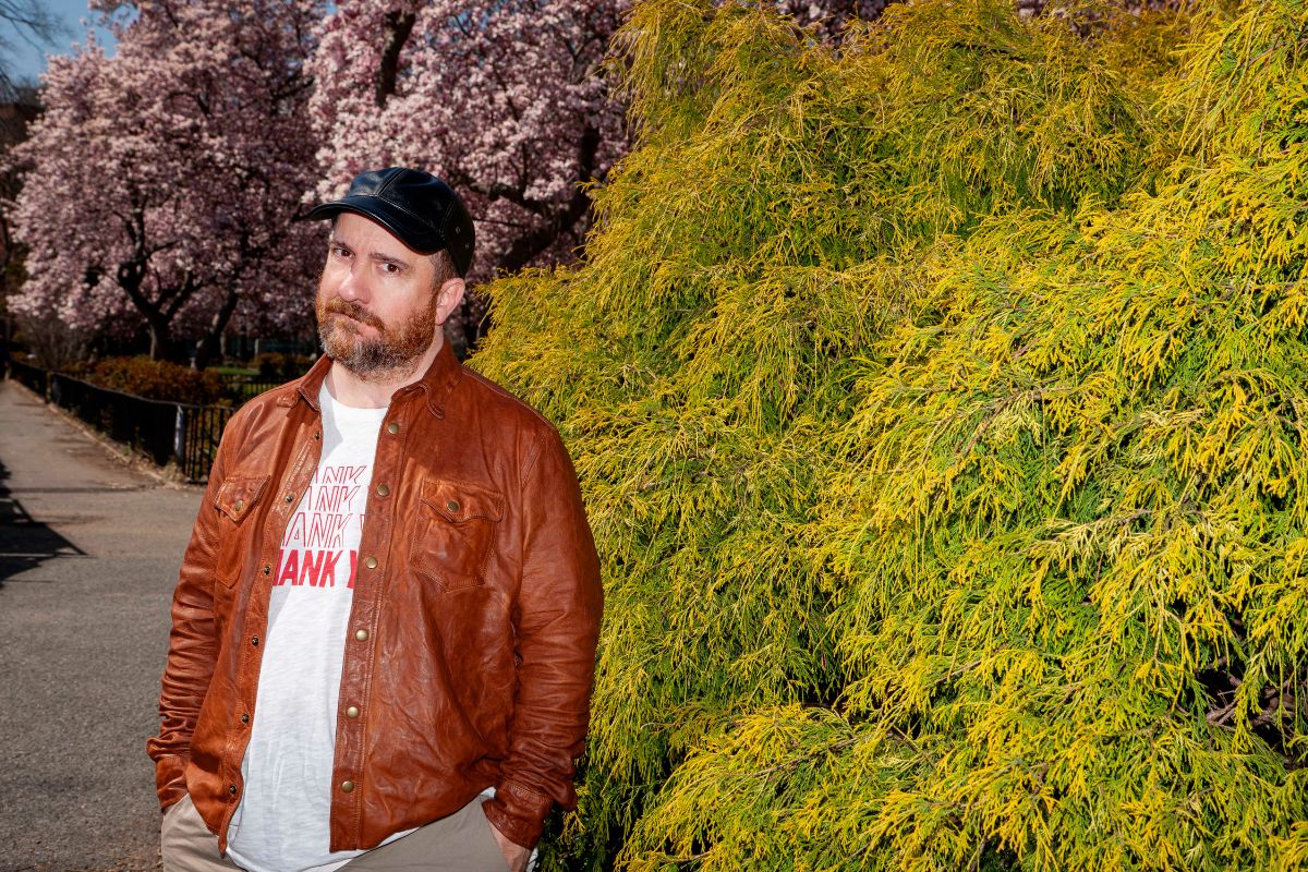 Picture of a man wearing a black hat standing next to green plants