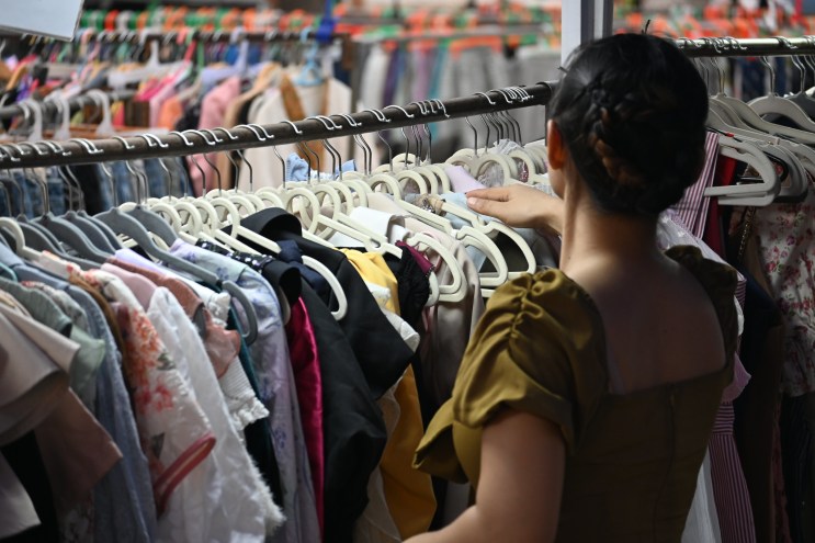 view from behind of a woman looking through racks of clothing at a thrift store