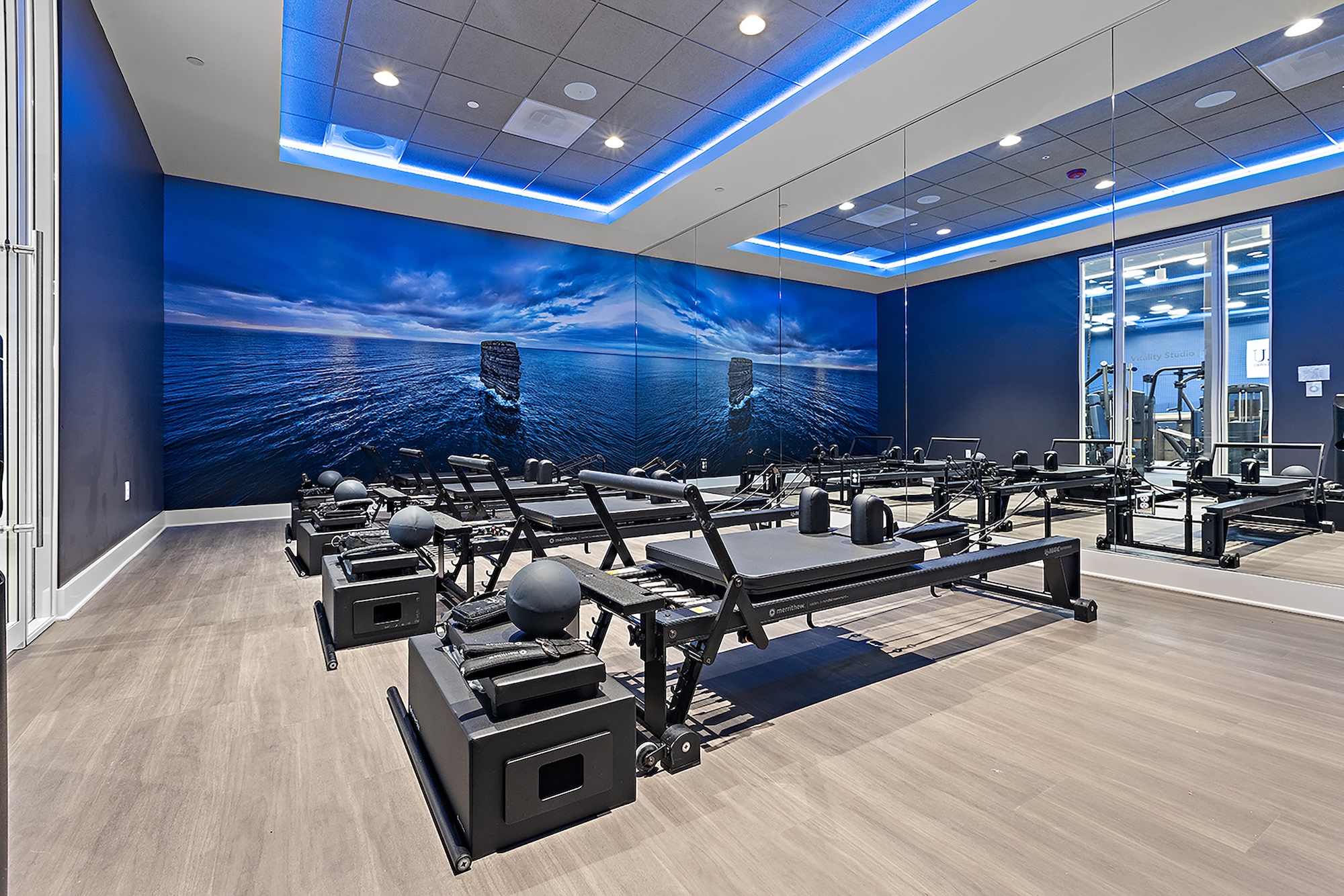 a room with eight pilates reformers and a wall with a photo of an island in the ocean