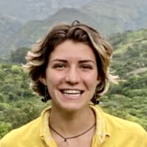 headshot of a smiling woman with short dark hair, with mountains in the background
