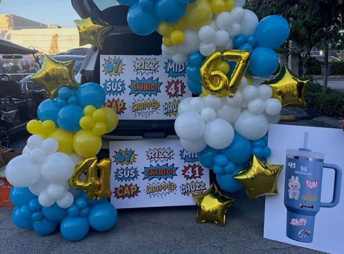 a photo of an open SUV trunk with white, blue, and gold balloons and posters with nonsense phrases like "67," "skibidi," and "rizz"