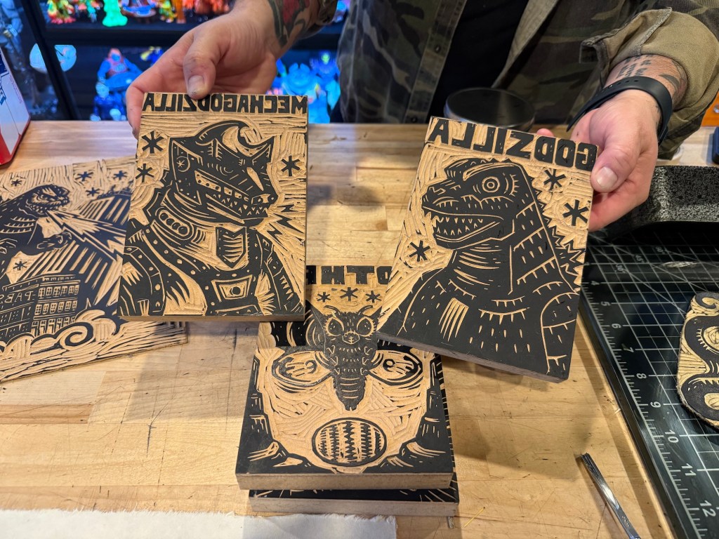 photo of two hands holding wooden animated stencils of Godzilla and Mechagodzilla