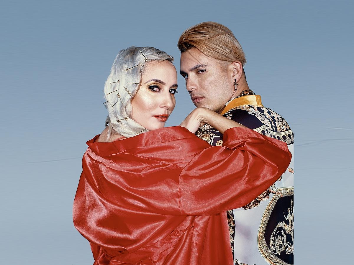 A woman and a man posing for the camera against a light blue background.