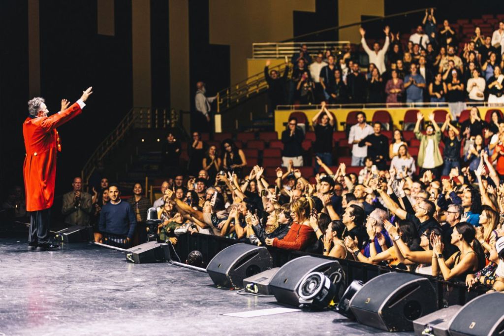 A singer on stage in front of a crowd raising his hand.