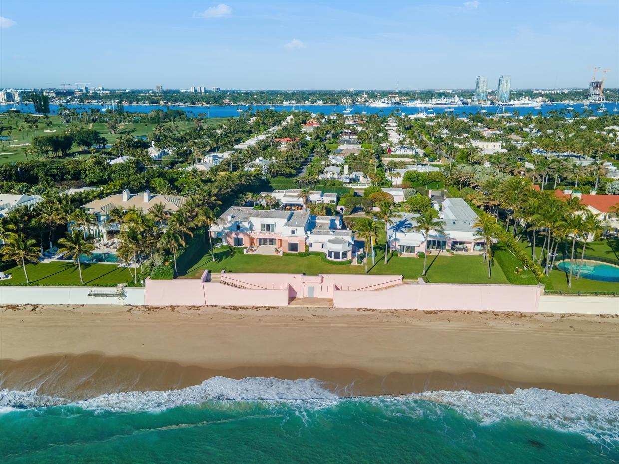 A sprawling 2-acre estate with multiple pink buildings sits behind a massive pink seawall and turquoise waters lapping on the coast.
