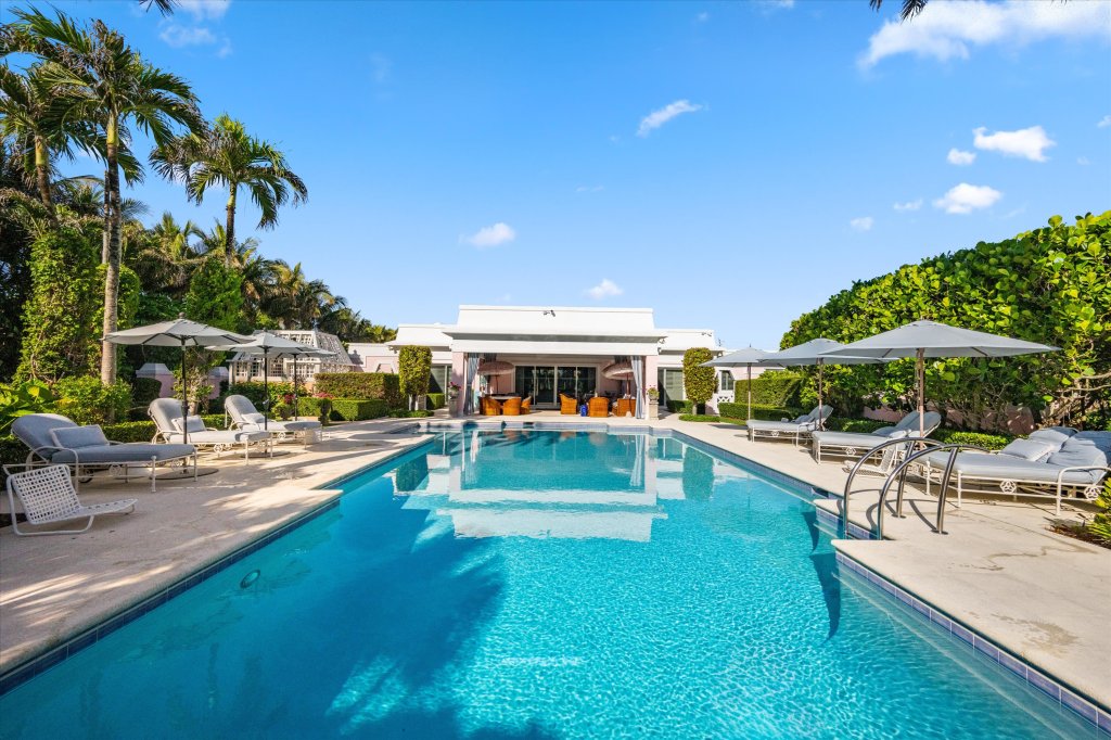 a resort-style pool is lined with reclining lounge chairs and umbrellas