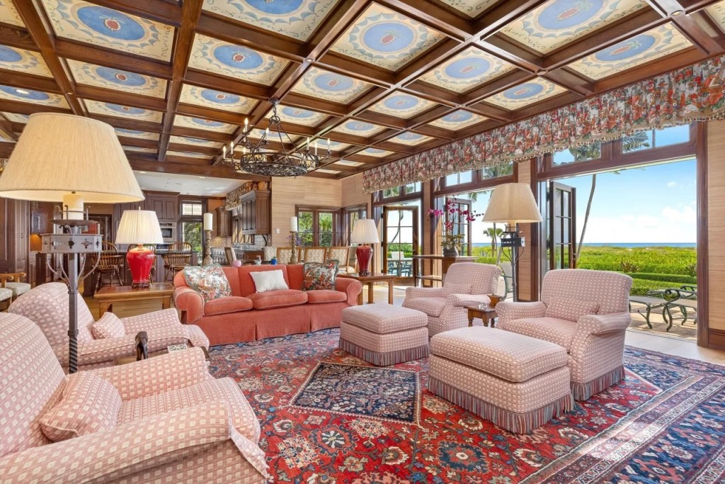 multiple arm chairs and a couch rest on a massive rug with French doors open to the beach