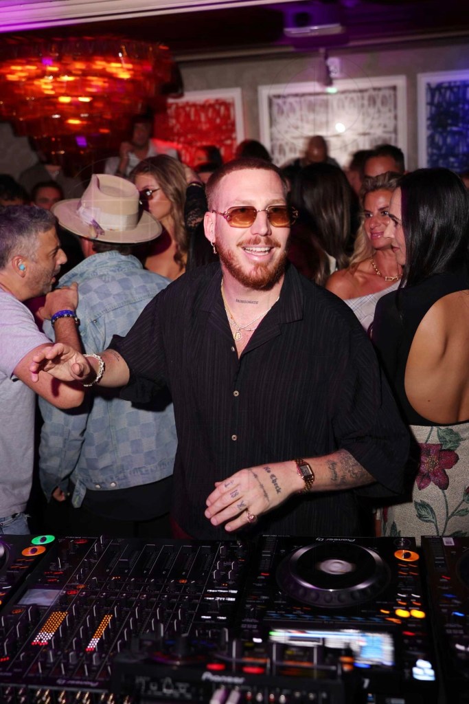 photo of a DJ at a booth with partygoers standing behind him