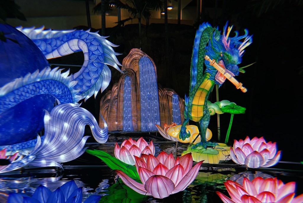 photo of illuminated sculptures of a dragon, waterfall, lotus flowers and lily pads on water