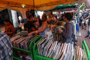 photo of people rifling through books on carts underneath a tent at a book fair