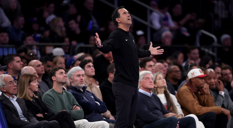An NBA basketball coach dressed all in black stands on the sideline with his arms outstreched as if in supplication