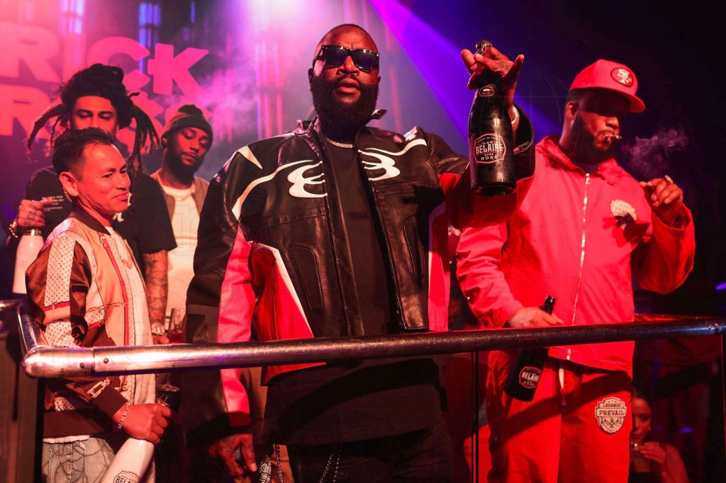photo of rapper Rick Ross holding up a bottle of rosé onstage with his entourage