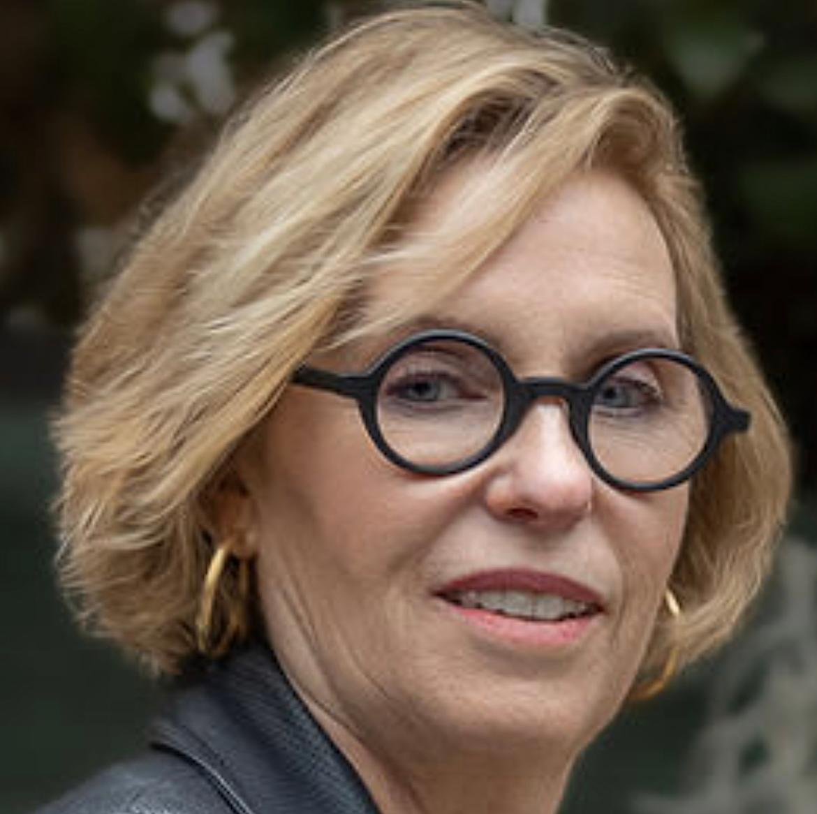 three-quarters headshot of a woman with a blond bob haircut and round-rimmed glasses