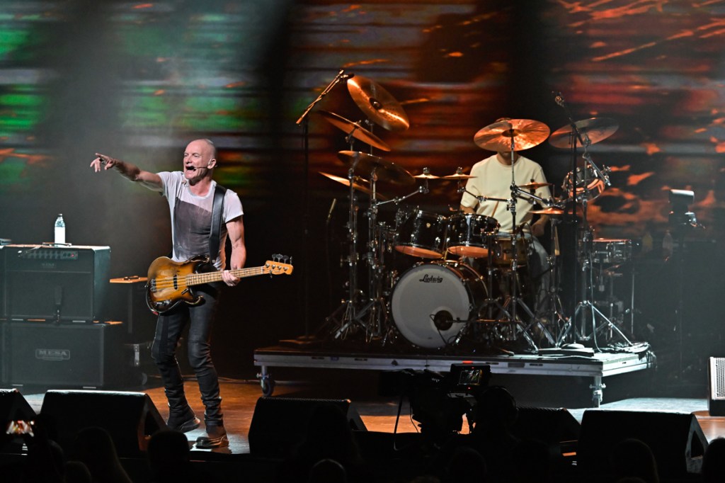 Photo of Sting and his band on stage under brown lights.