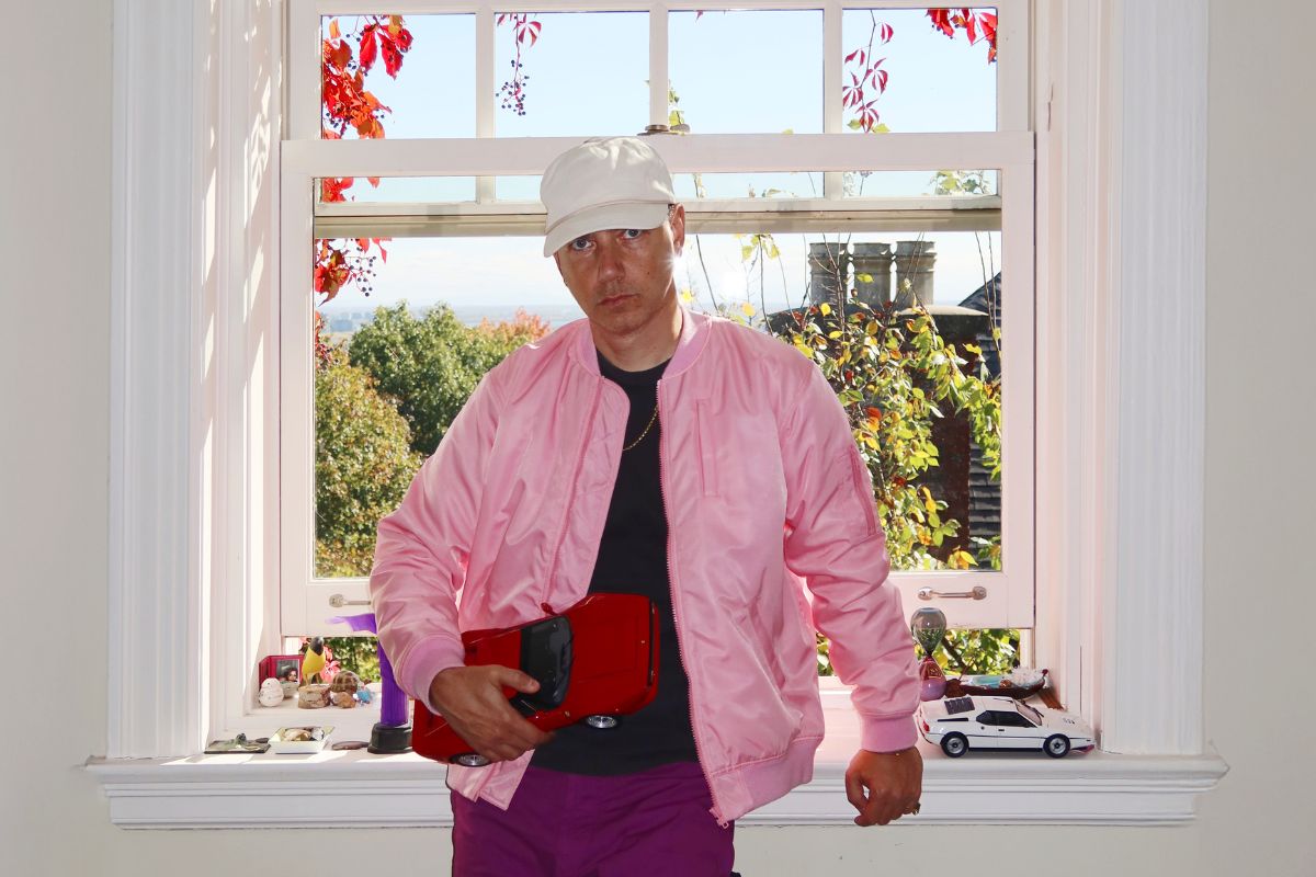 A photo a man sitting by a window wearing a pink jacket.