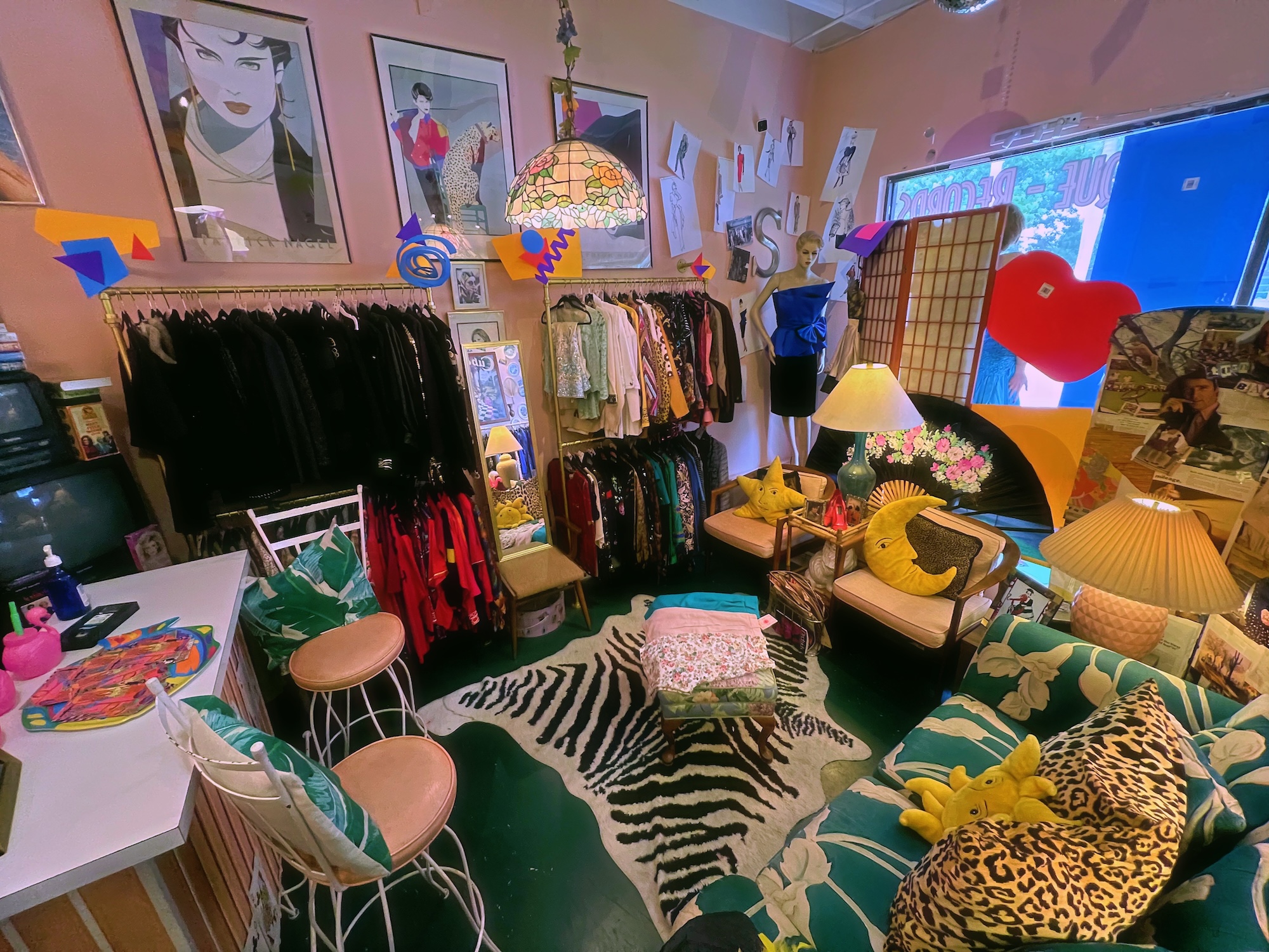 photo of a vintage shop with pastel-pink walls, teal-and-white couches, racks of clothing, and framed posters on the walls