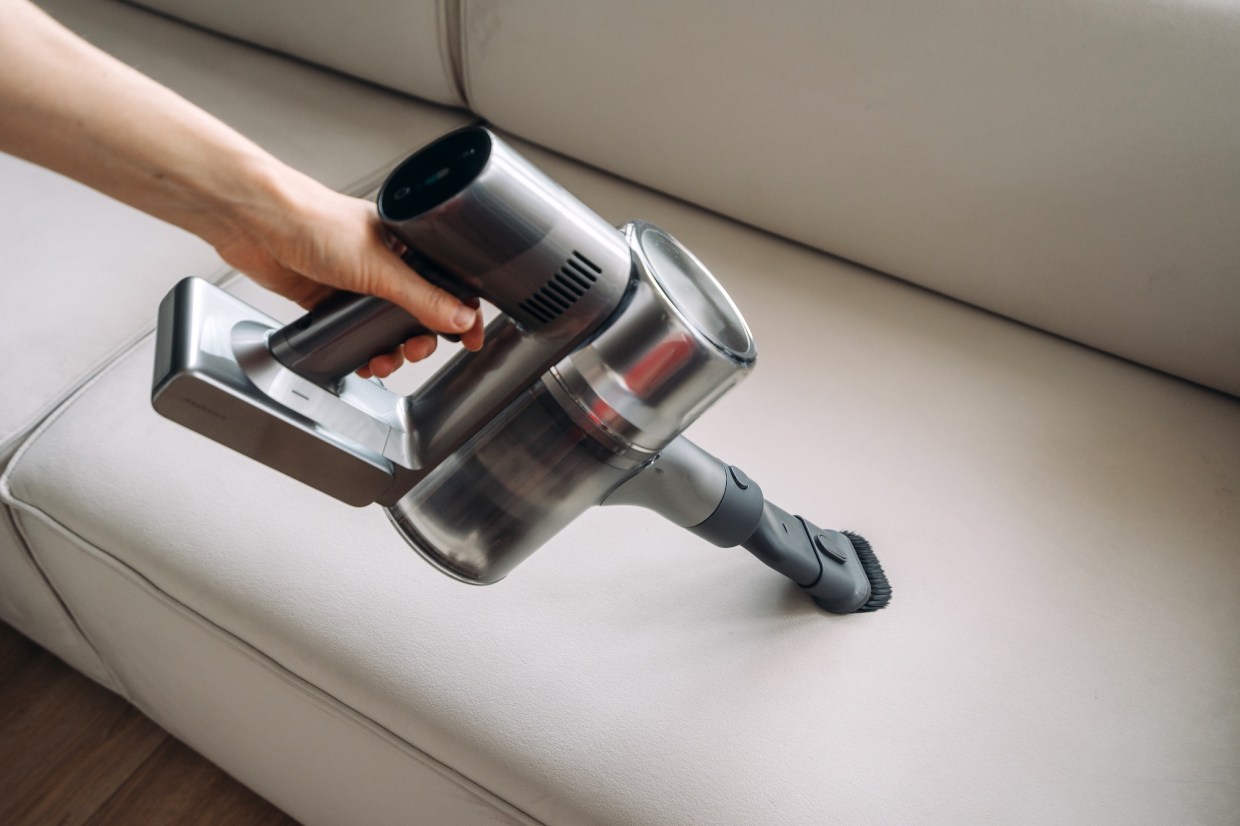 photo showing woman's arm grasping a handheld vacuum cleaner as if cleaning an off-white couch