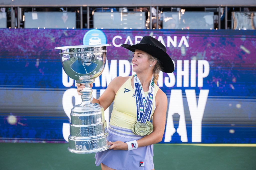 photo of Anna Leigh Waters in a black cowboy hat wearing a medal and holding up a huge trophy