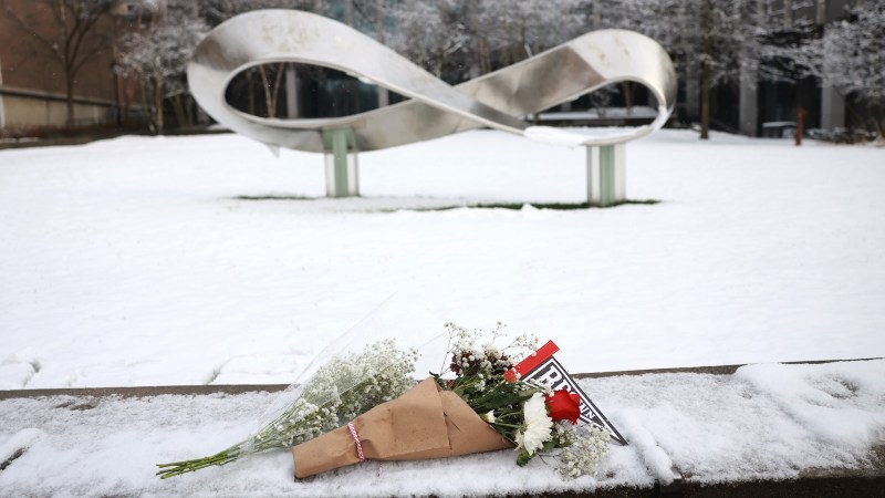 two bouquets of flowers placed atop a low stone wall dusted with snow. in the background, a large sculpture in the shape of the infinity symbol / möbius strip