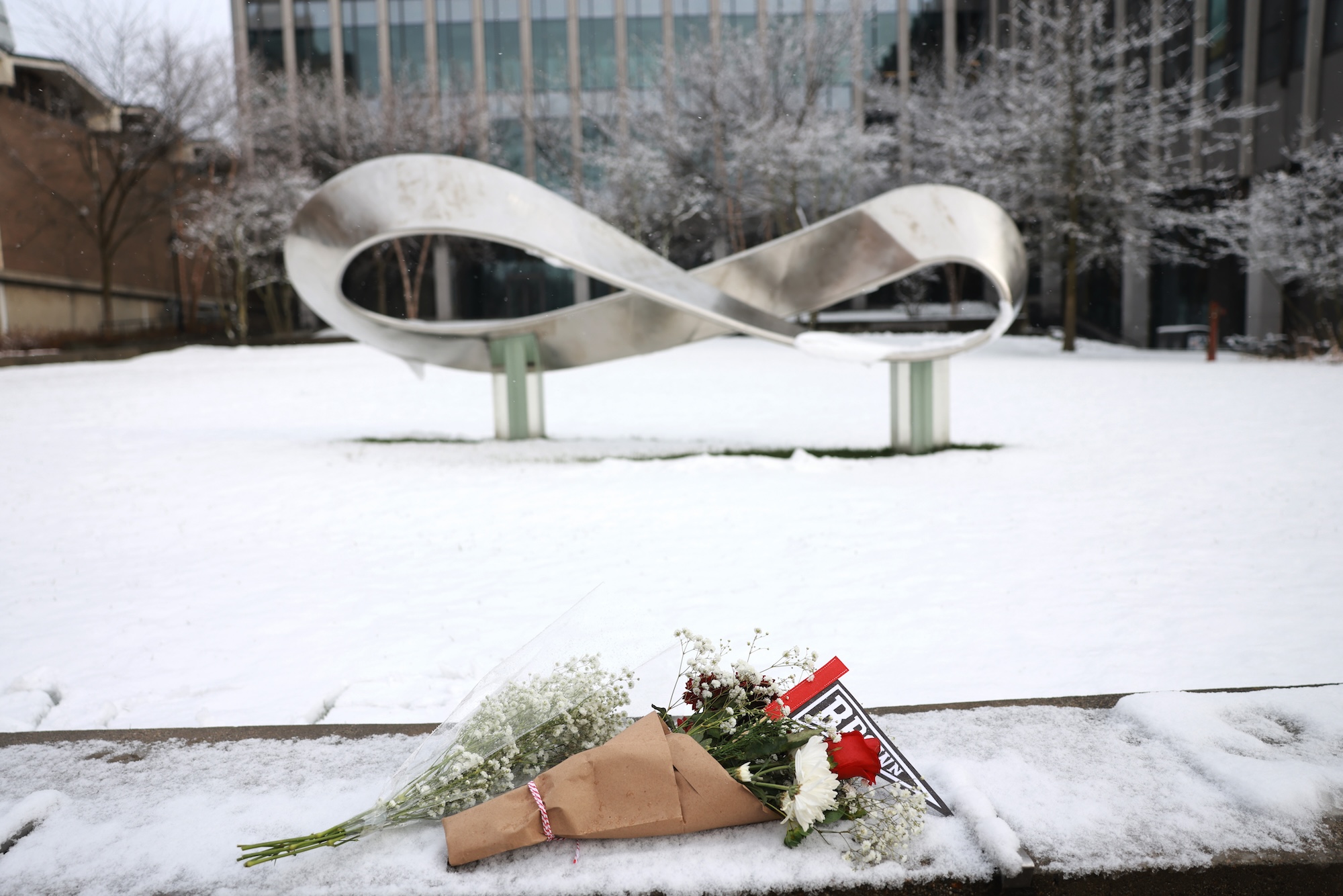 two bouquets of flowers placed atop a low stone wall dusted with snow. in the background, a large sculpture in the shape of the infinity symbol / möbius strip