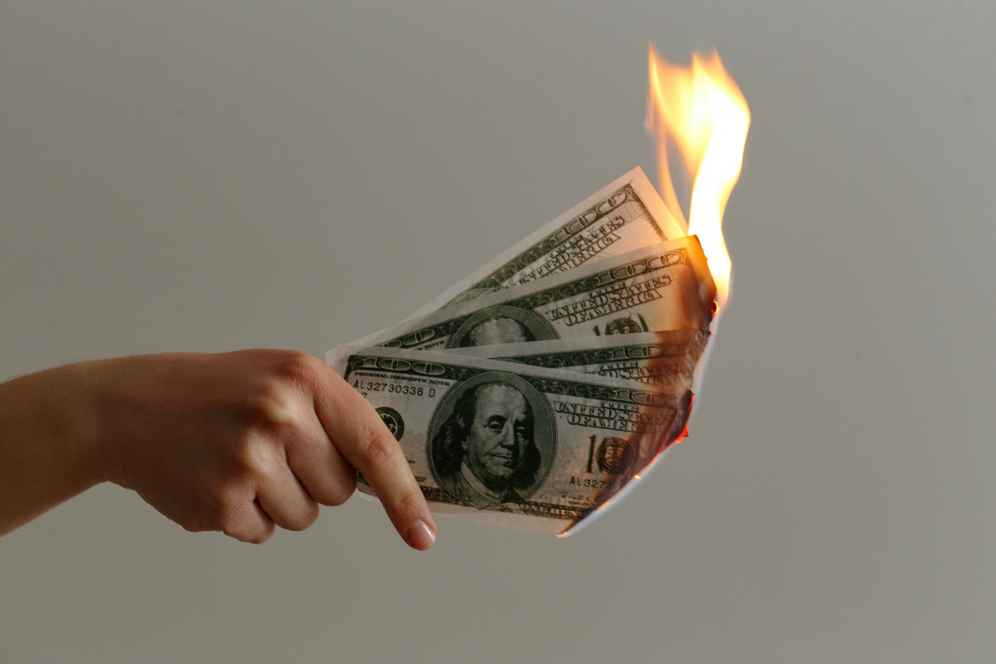 photo of a hand holding four one-hundred-dollar bills on fire
