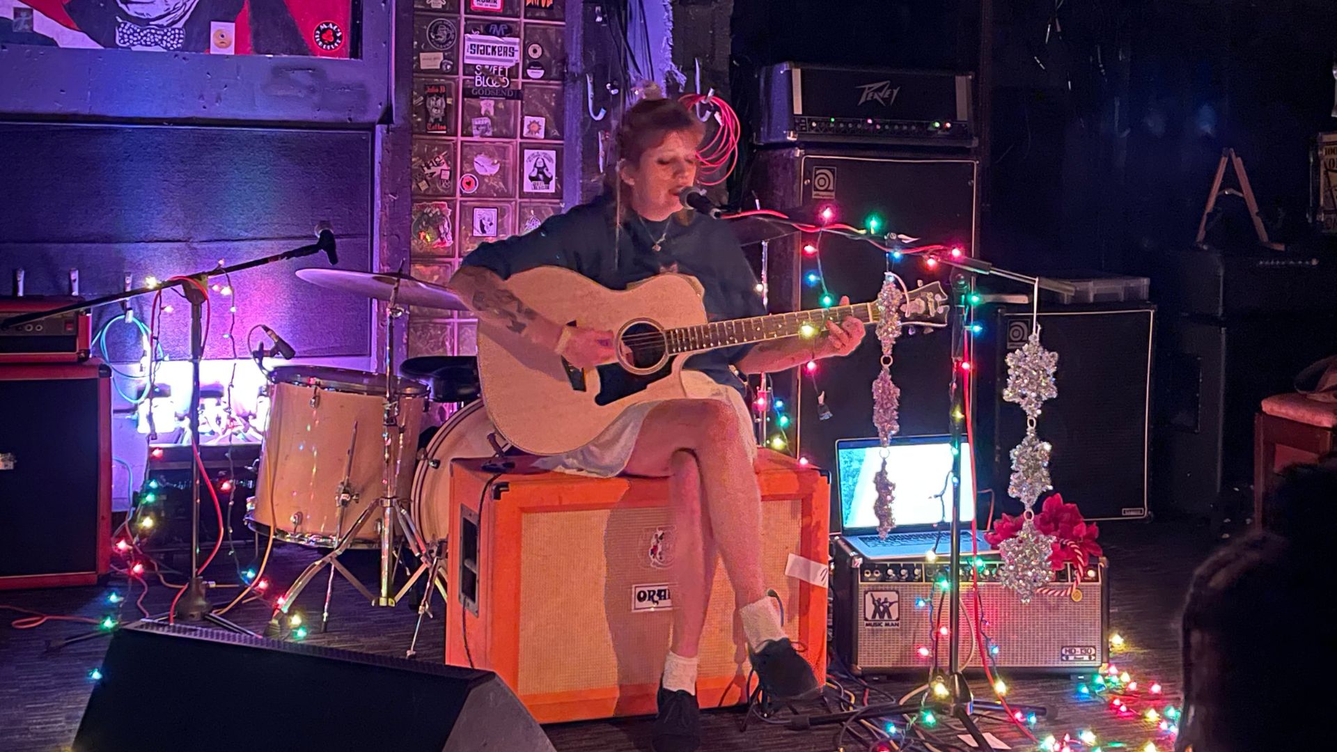 A photo of a woman playing a guitar sitting on an amplifier.