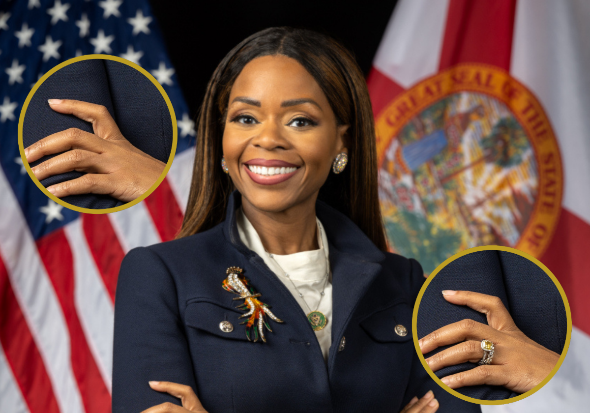 A woman in a navy blazer stands with her arms crossed in front of U.S. and Florida flags. Two circular insets zoom in on her hands, one highlighting a ring and another a bare finger.